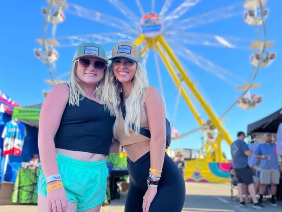 Cornhole festival goers in front of large Ferris wheel.